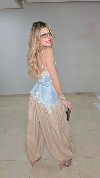Woman wearing a light blue top and beige pants with a pink clutch in an indoor setting.