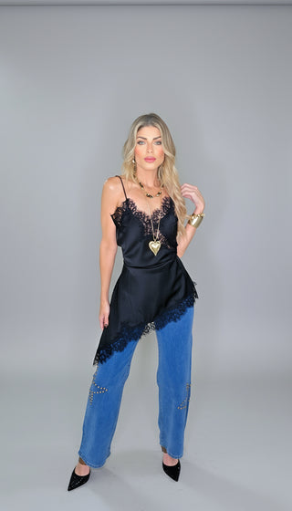 Woman in a black lace top and blue jeans standing in front of a decorated Christmas tree.